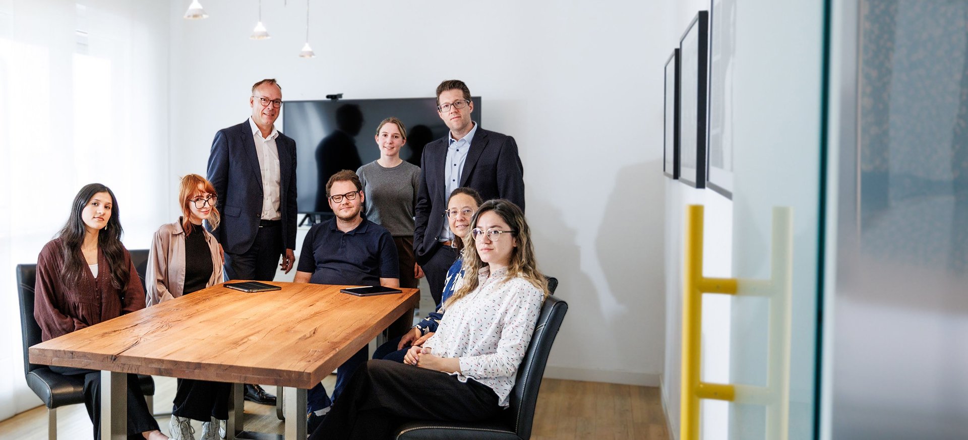 Lächelndes Team aus sieben Mitarbeitern in einem modernem Büro am Besprechungstisch.