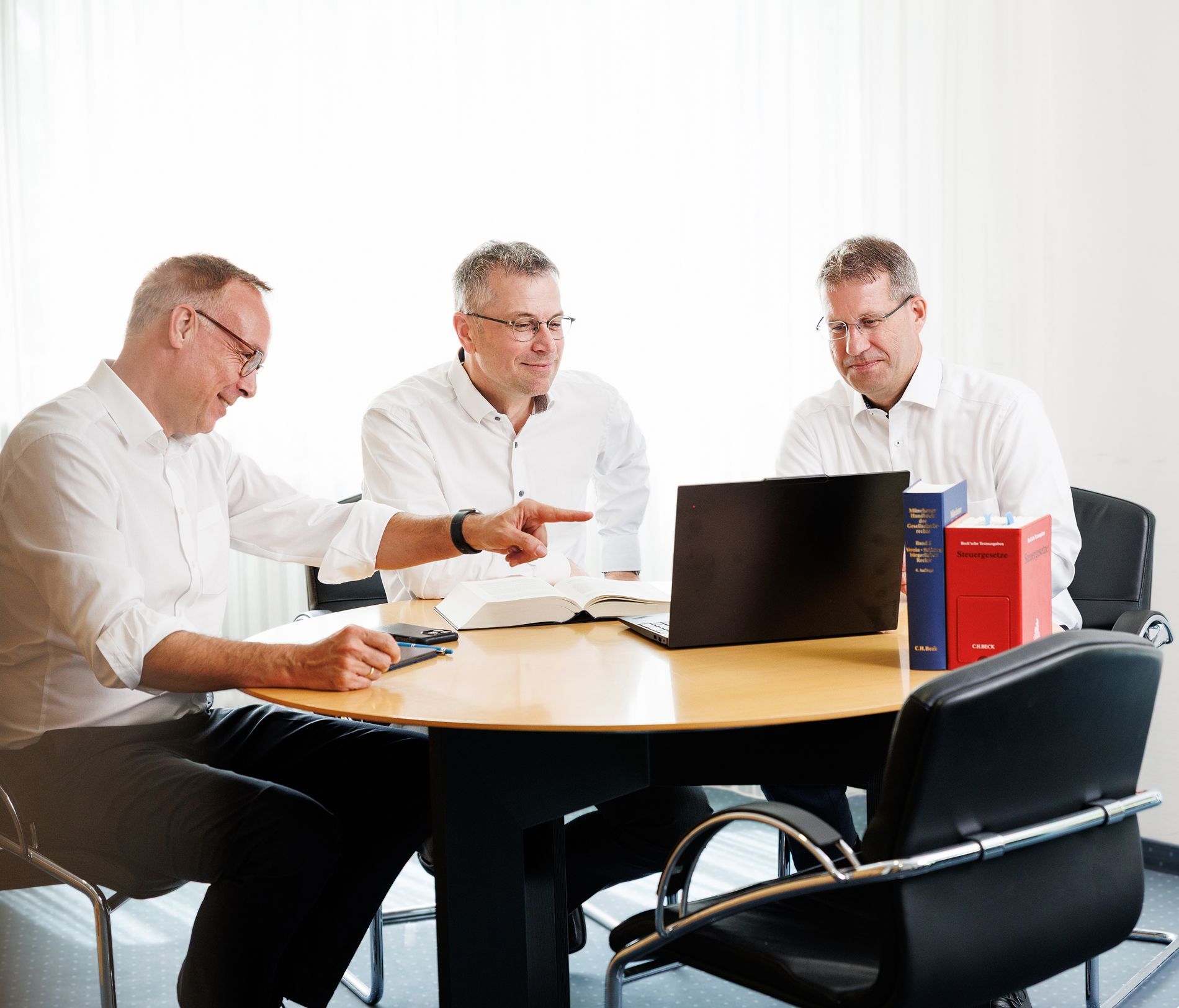 Vier junge Berufstätige in Business-Kleidung stehen nebeneinander in einem modernen Bürogebäude und blicken in die Kamera.