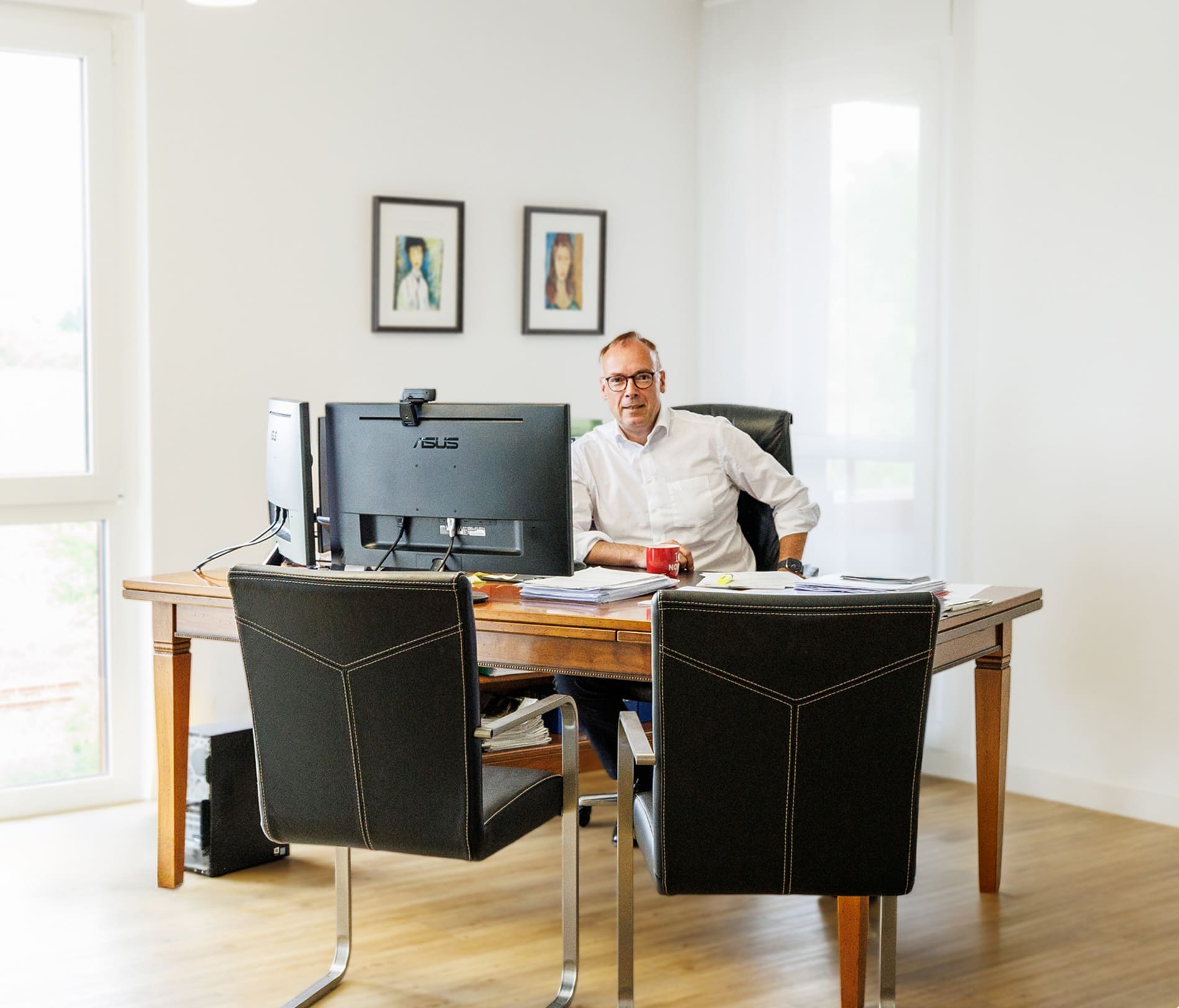 Ein Mann sitzt an einem Schreibtisch mit zwei Monitoren im hellen Büro.