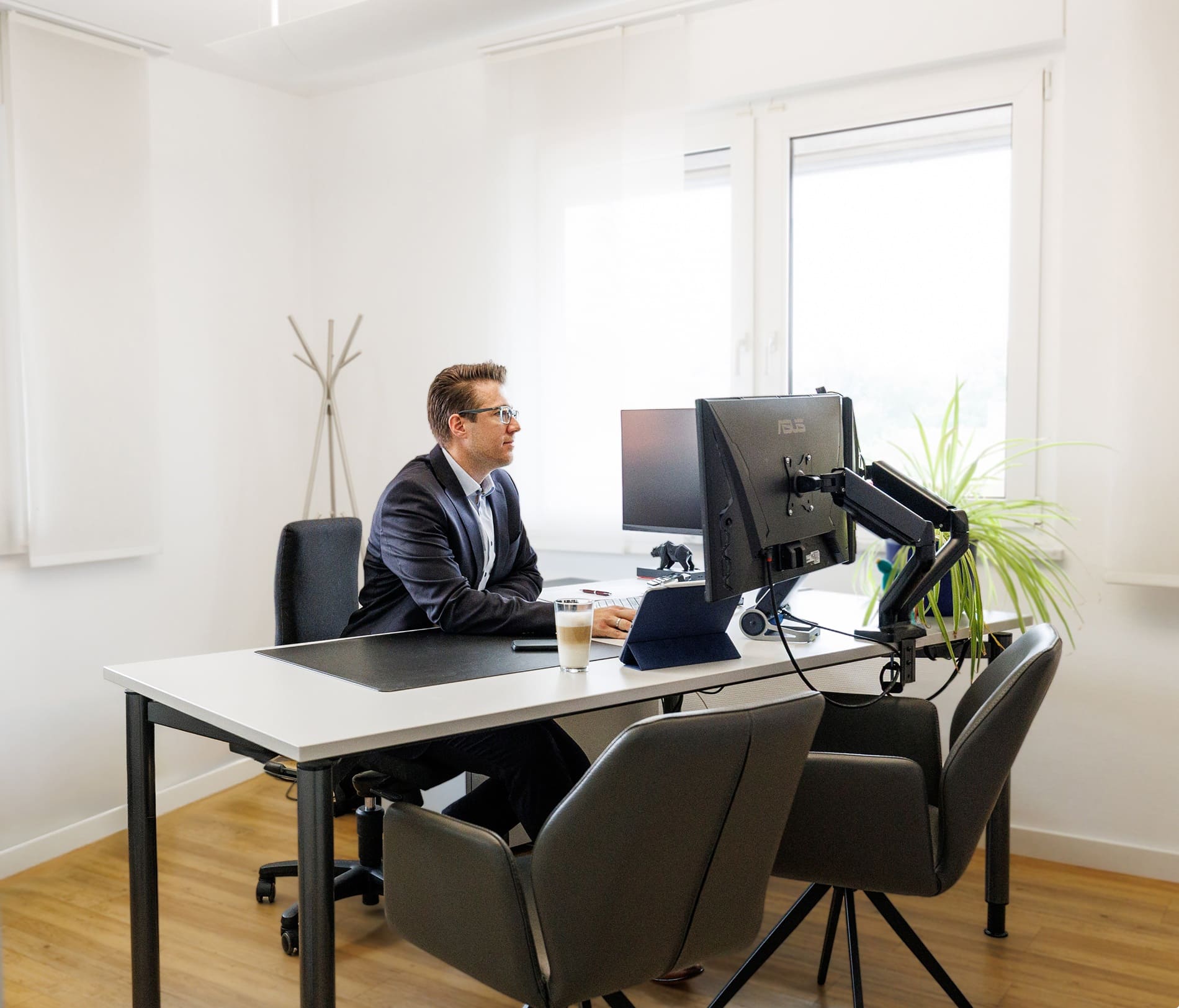 Berater im Anzug arbeitet am Schreibtisch mit zwei Asus-Monitoren im hellen Büro.