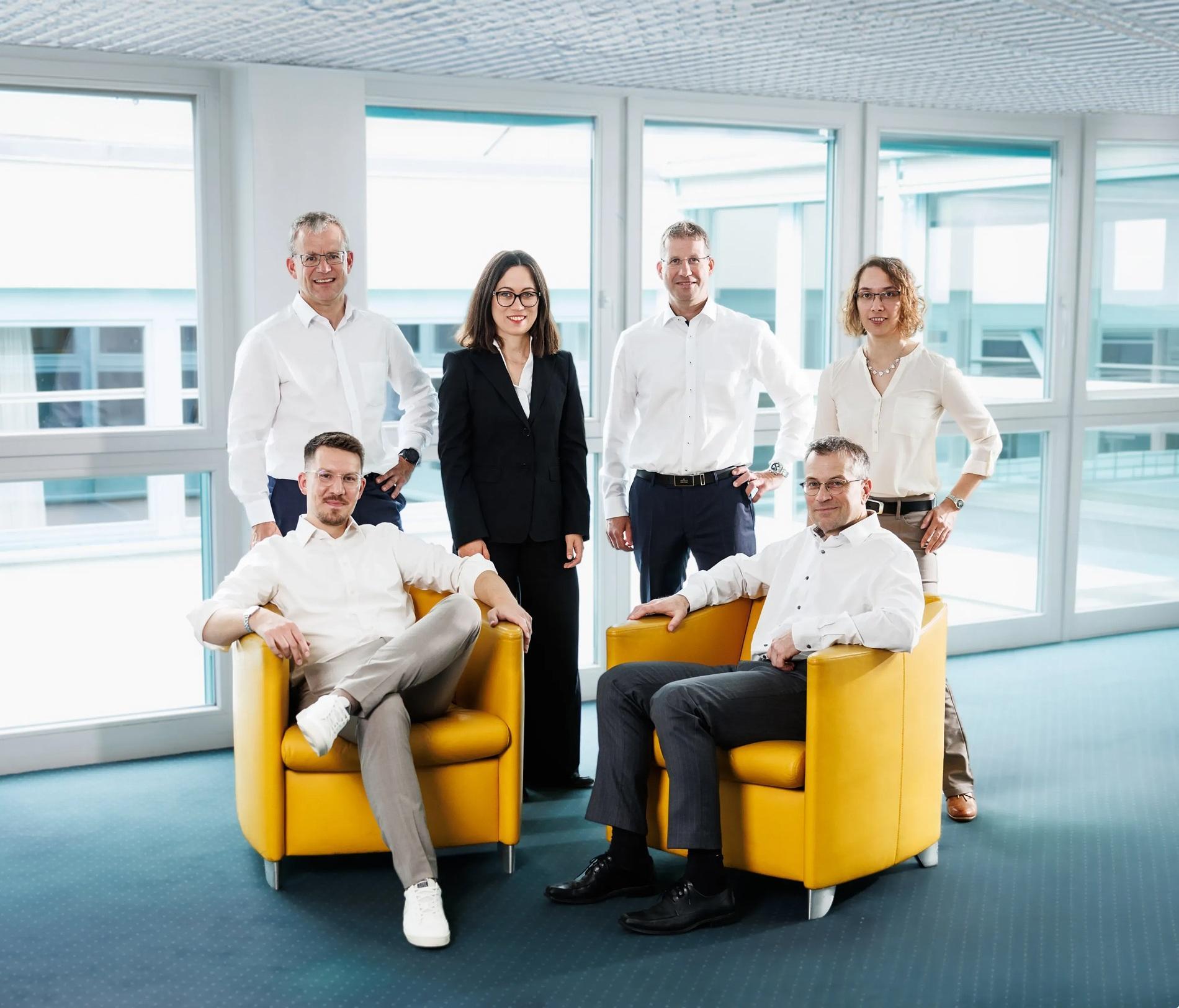 Das Team von FRT Partner lächelt in einem hellen Büro mit gelben Sesseln.