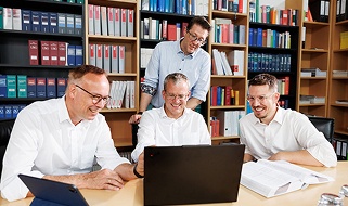 Vier lächelnde Männer besprechen gemeinsam Inhalte auf einem Laptop im Büro.