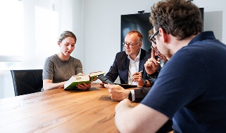 Vier Mitarbeiter besprechen Fachliteratur bei einem Meeting am Holztisch.