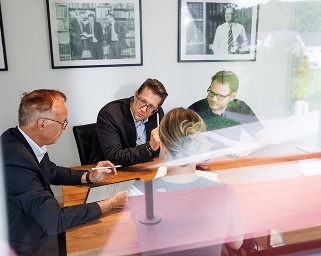 Drei Kollegen im Business-Outfit besprechen Unterlagen an einem Holztisch im Büro.