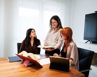 Drei Frauen besprechen Dokumente bei einem Meeting an einem Holztisch mit iPad.